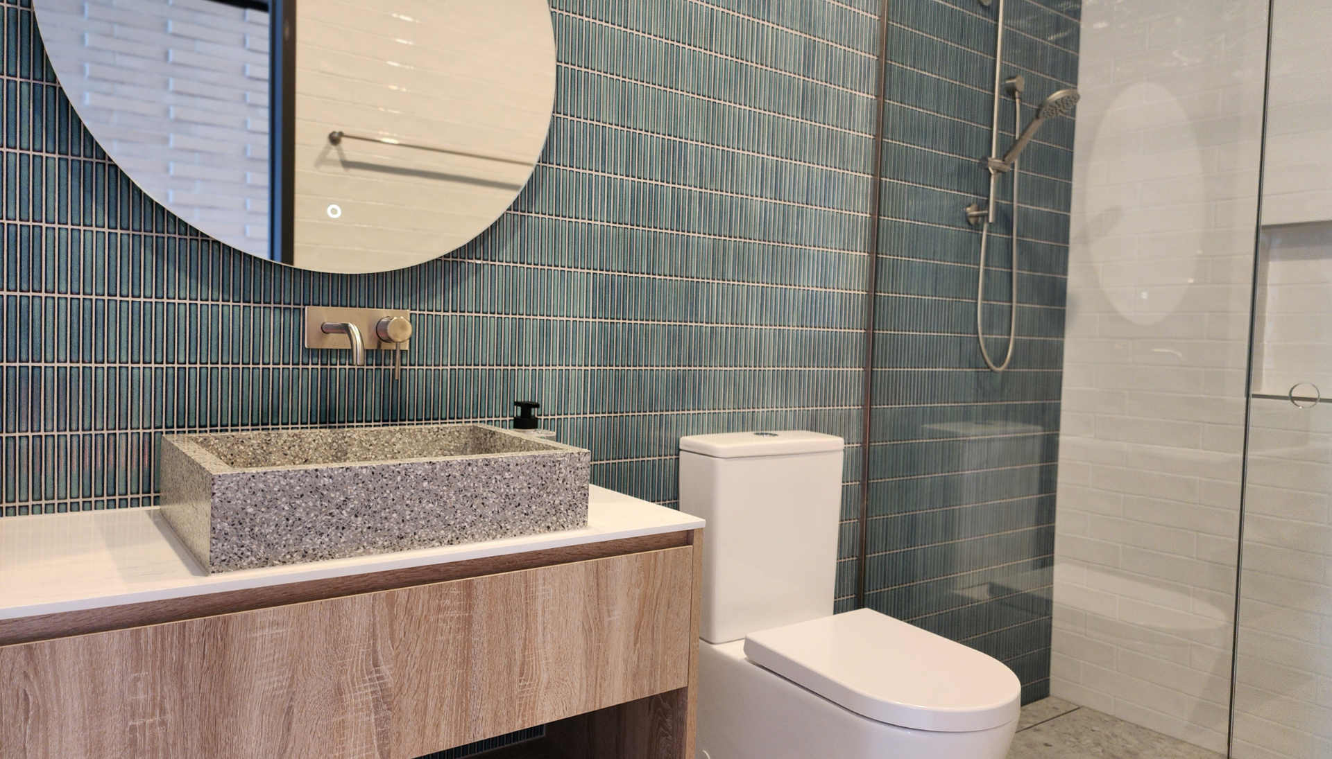 Blue-green vertical stack bond wall tiles in a bathroom with a round mirror